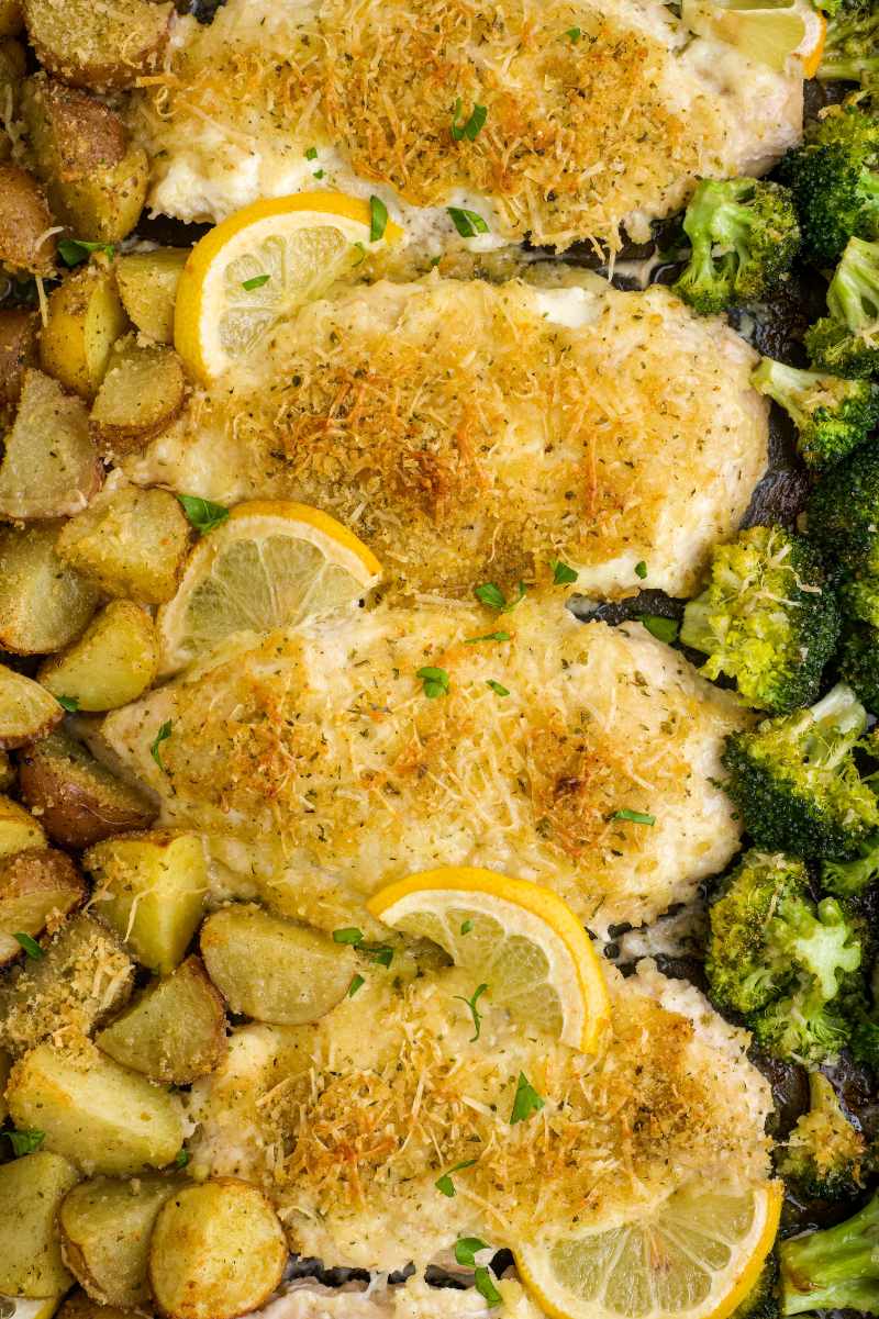 Tight view of lemon chicken topped with parmesan, broccoli florets and baby potatoes nestled on either side.