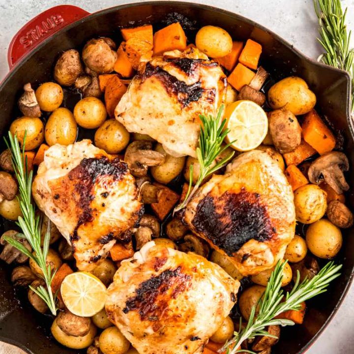 Top view of a lemon chicken skillet family dinner with four chicken thighs on top of a bed of fall veggies in an enameled cast iron skillet.