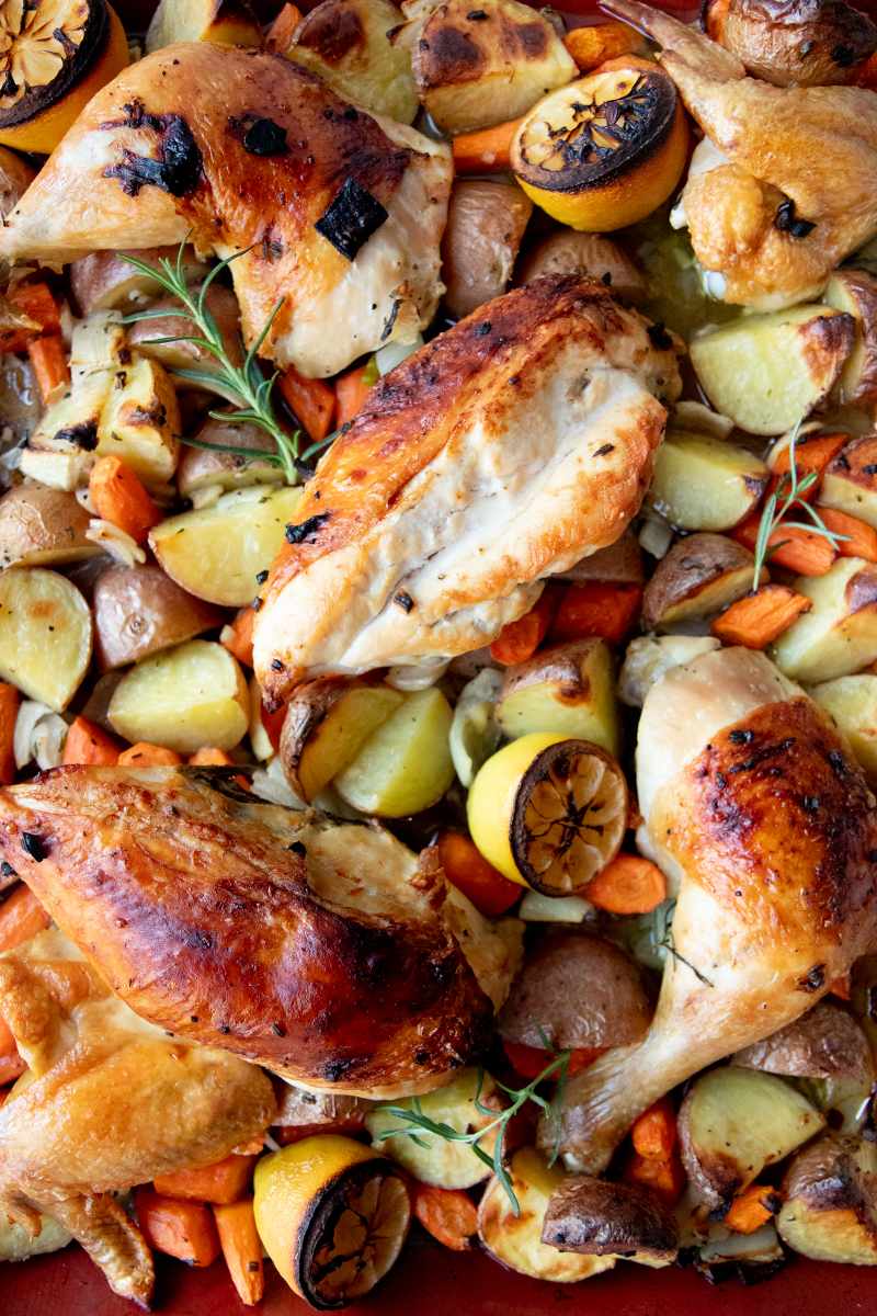 Close view of roasted chicken pieces and root veggies such as potatoes and carrots.