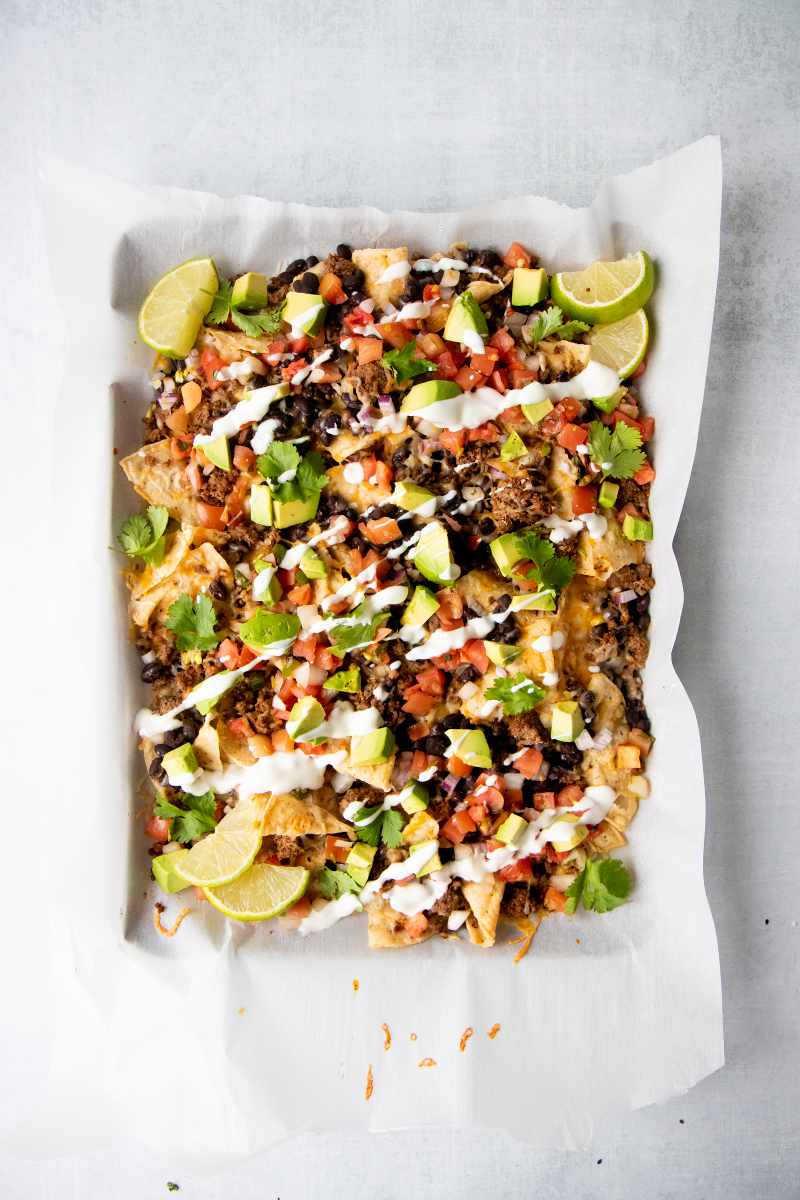 Overhead of a parchment paper lined half-sheet pan piled high with loaded ground beef nachos.