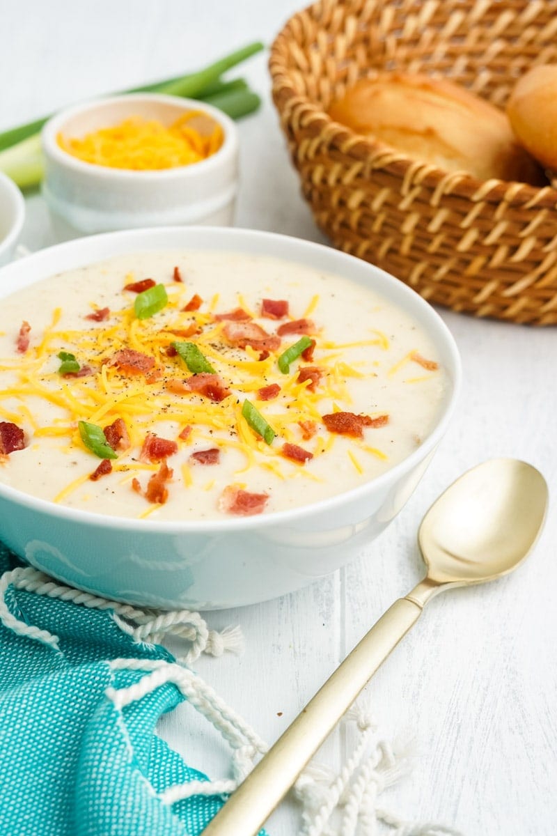 A spoon rests on a table beside a full bowl of mashed potato soup with loaded toppings.