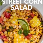 A serving bowl of finished mexican street corn salad garnished with cilantro leaves and a lime wedge. A text overlay reads, "Mexican Street Corn Salad."