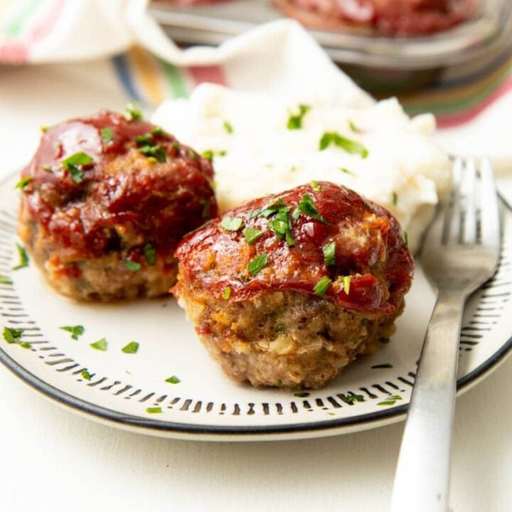 A glazed mini meatloaf is served on a white plate with a side of mashed potatoes and a second meatloaf.