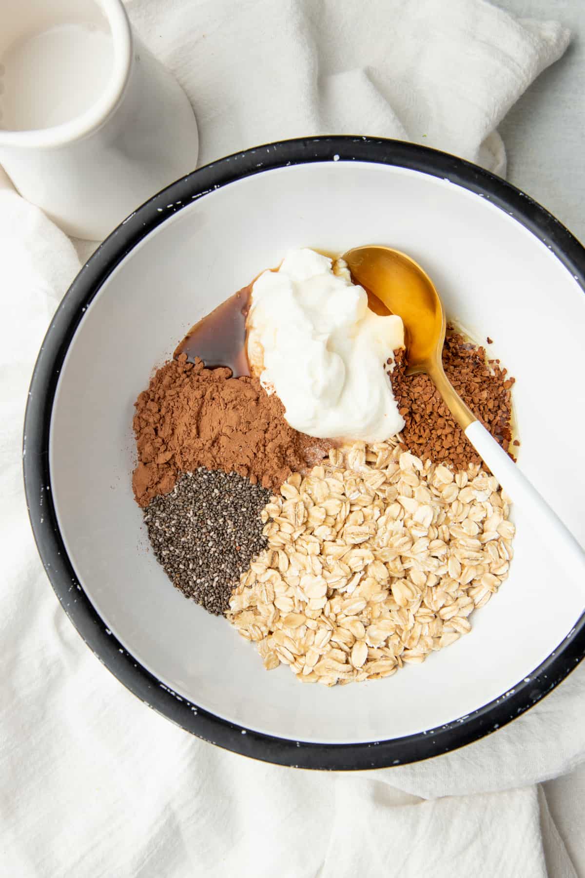 A golden spoon rests in a white bowl. Ingredients for oatmeal are arranged in the bowl.