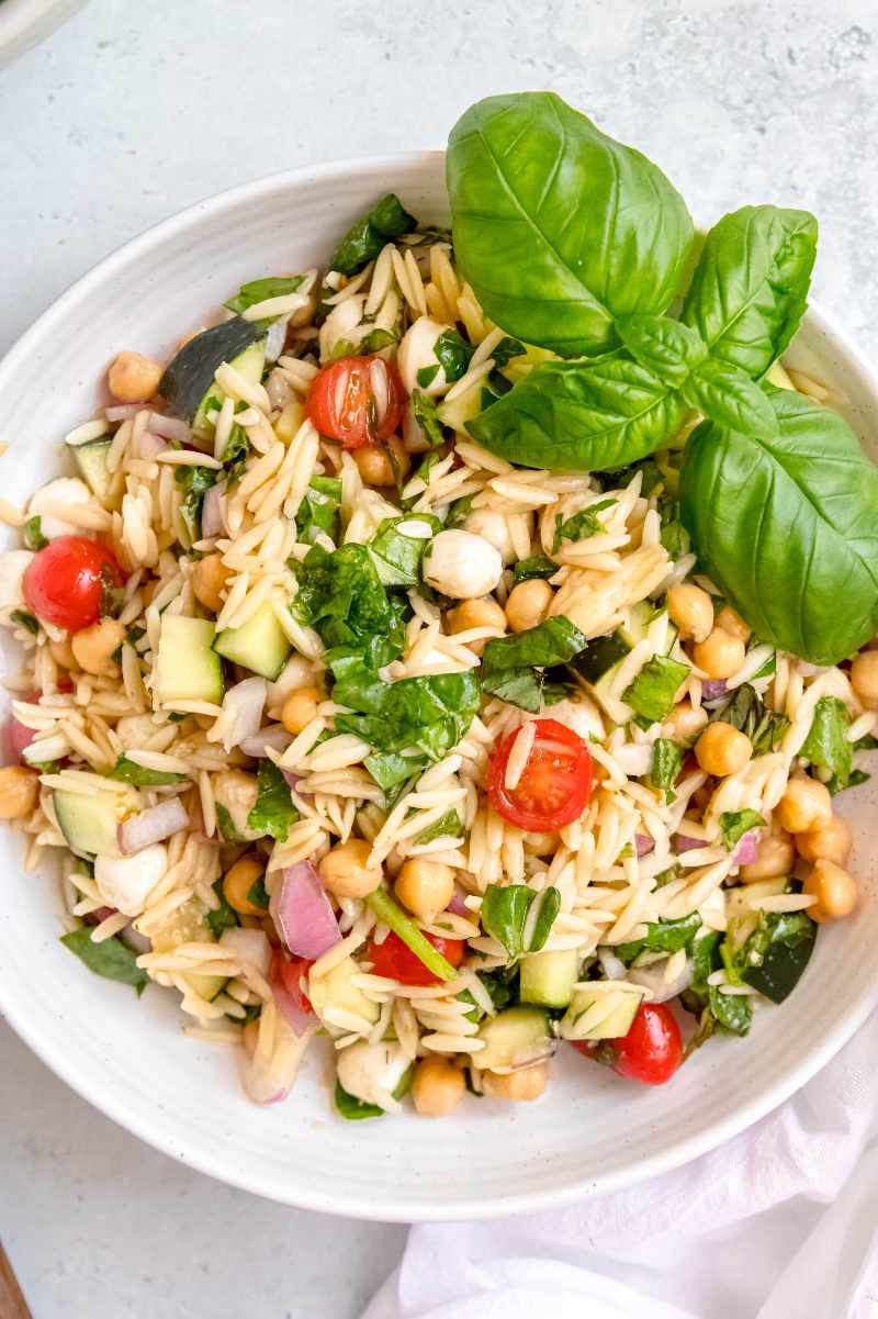 Overhead of orzo pasta salad in a white bowl on a light countertop.