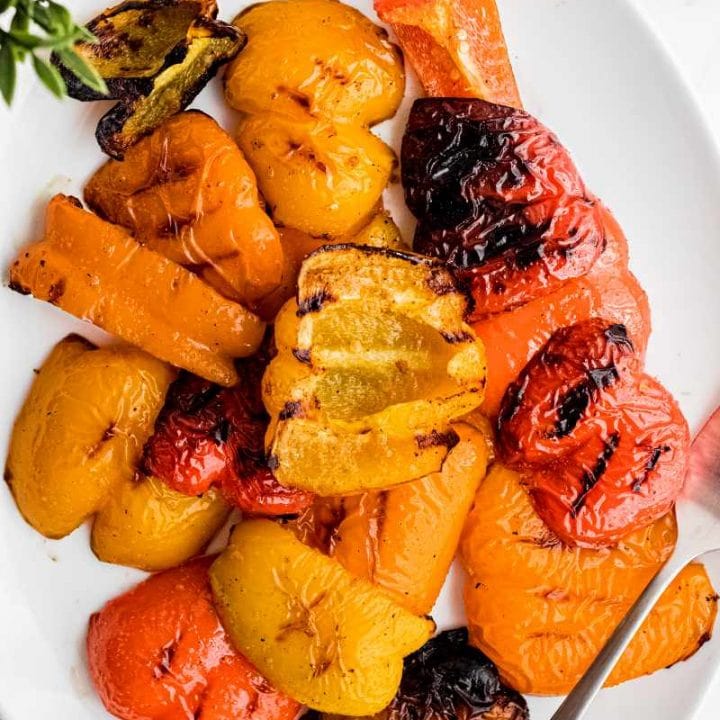 Grilled peppers on a large white oval platter with a serving fork.