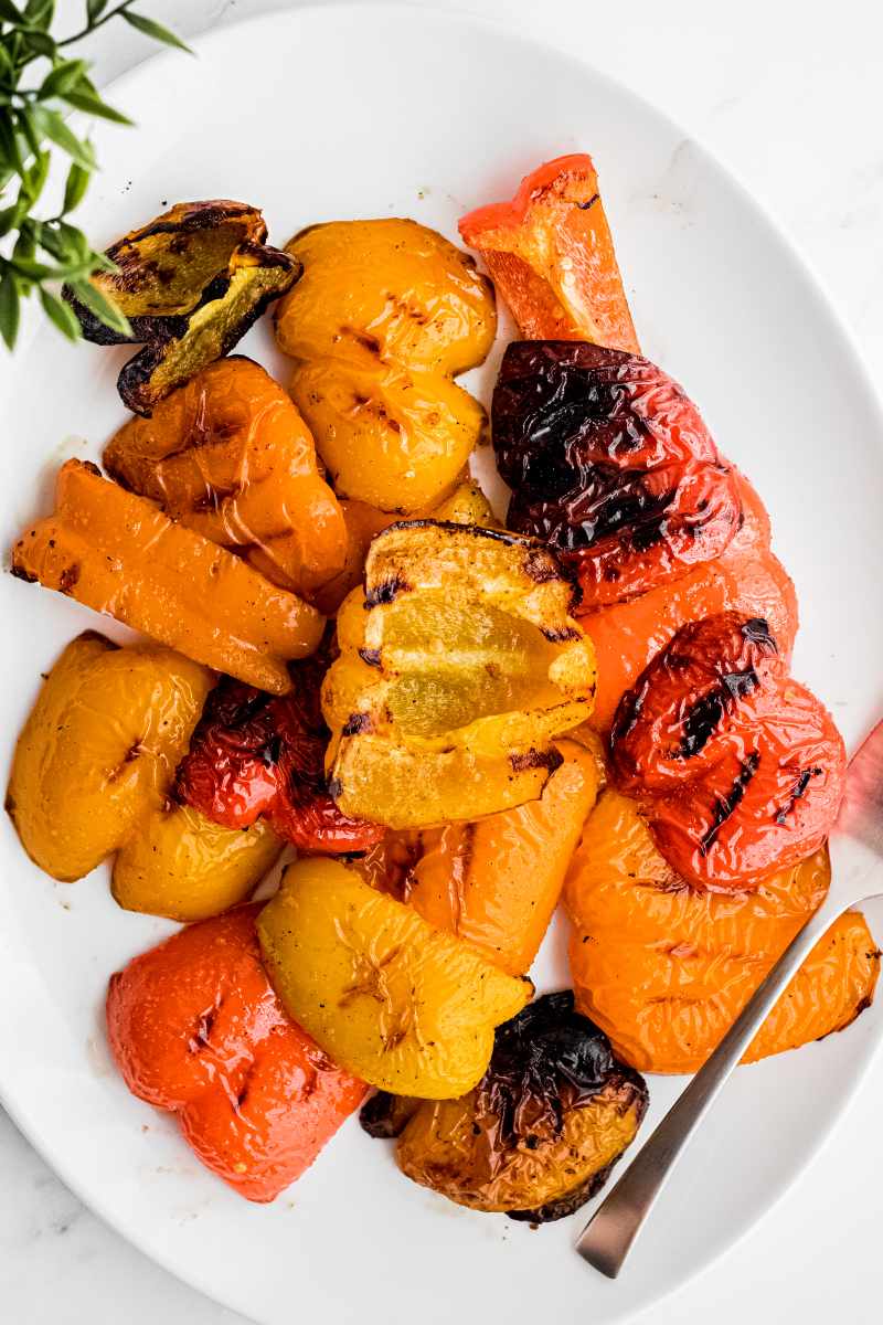 Grilled peppers on a large white oval platter with a serving fork.