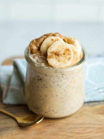 A small, gold, dessert spoon rests next to a jar of peanut butter banana overnight oats.