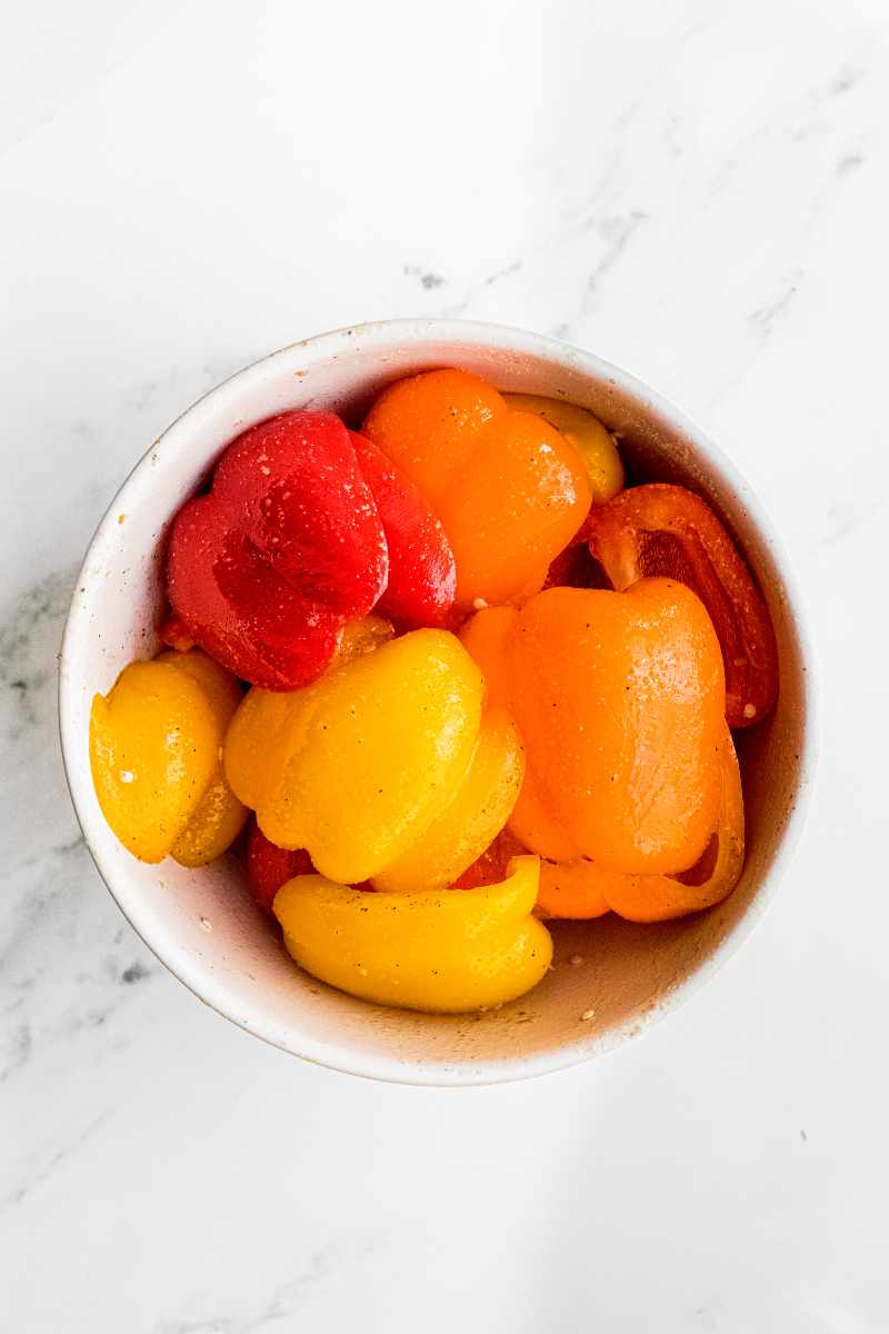 Bell pepper slices in a white bowl after being tossed with olive oil and dried seasonings.