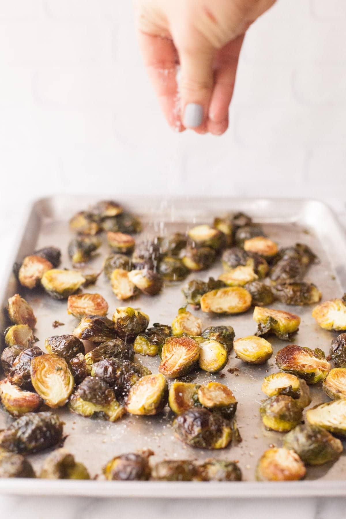 A hand sprinkles salt over a pan of roasted brussel sprouts