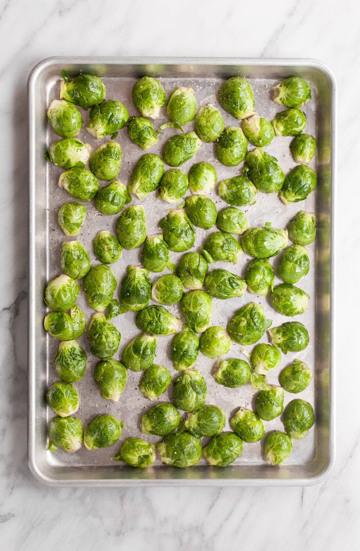 Cut Brussels sprouts are arranged in a single layer on a baking sheet, ready for roasting