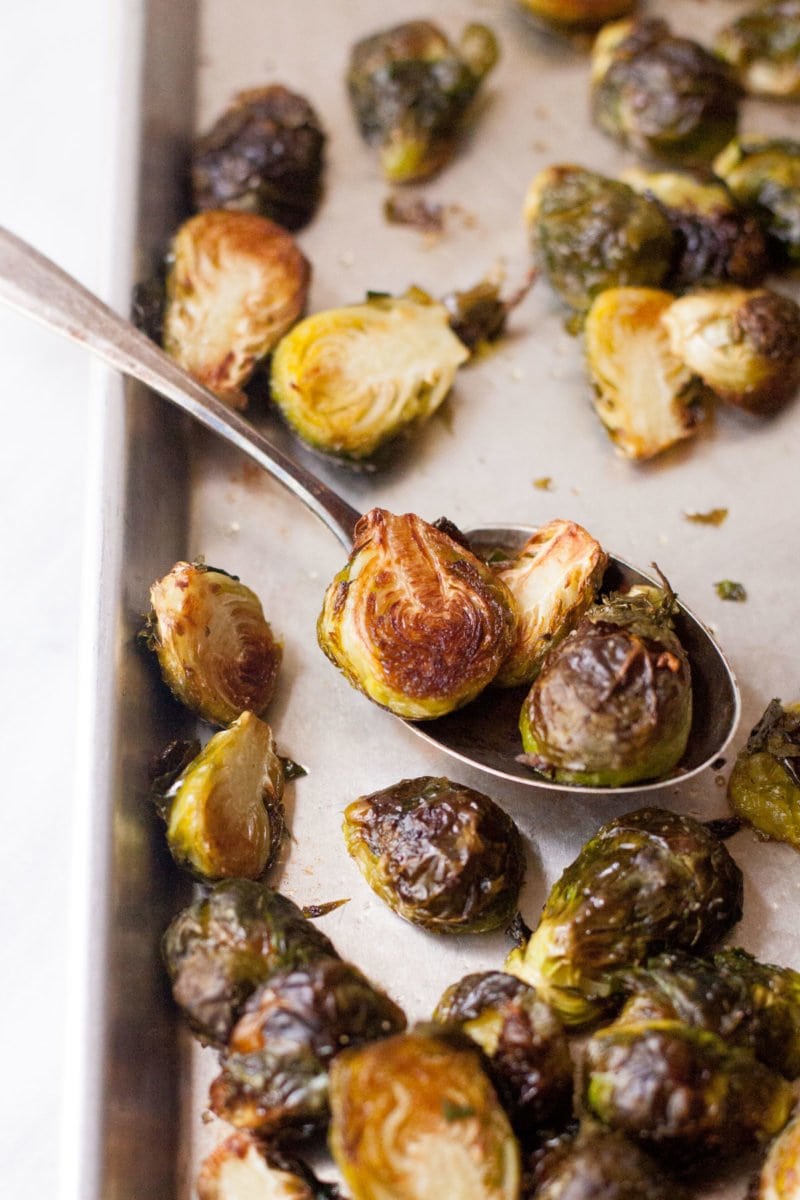 A spoon scoops roasted brussel sprouts from a sheet pan