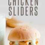 A chicken sandwich with slaw and ranch sauce sits on a wooden cutting board. A text overlay reads "Slow Cooker Sriracha Chicken Sliders."