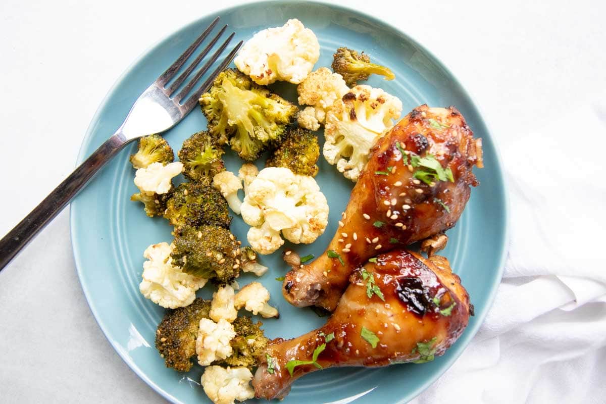 A blue dinner plate filled with two baked drumsticks and roasted broccoli and cauliflower.