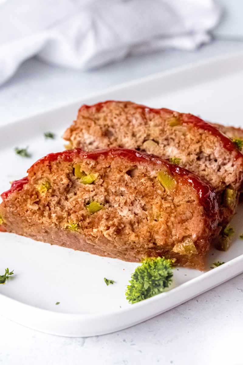 Two slices of meatloaf on a white plate garnished with fresh herbs.