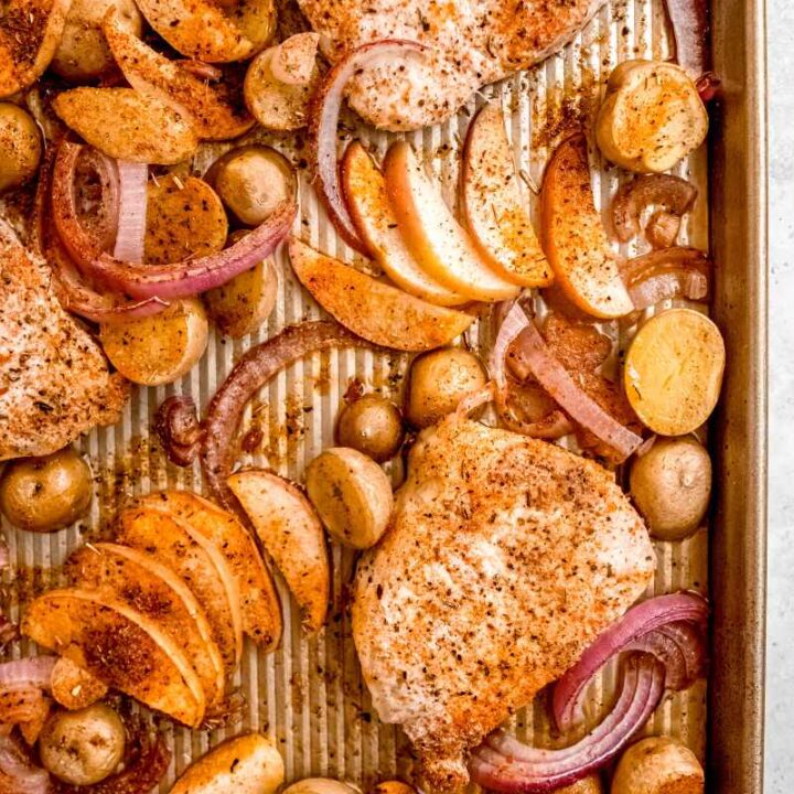 Overhead of pork chop dinner in a baking pan with seasoned chops, potatoes, and apple slices.