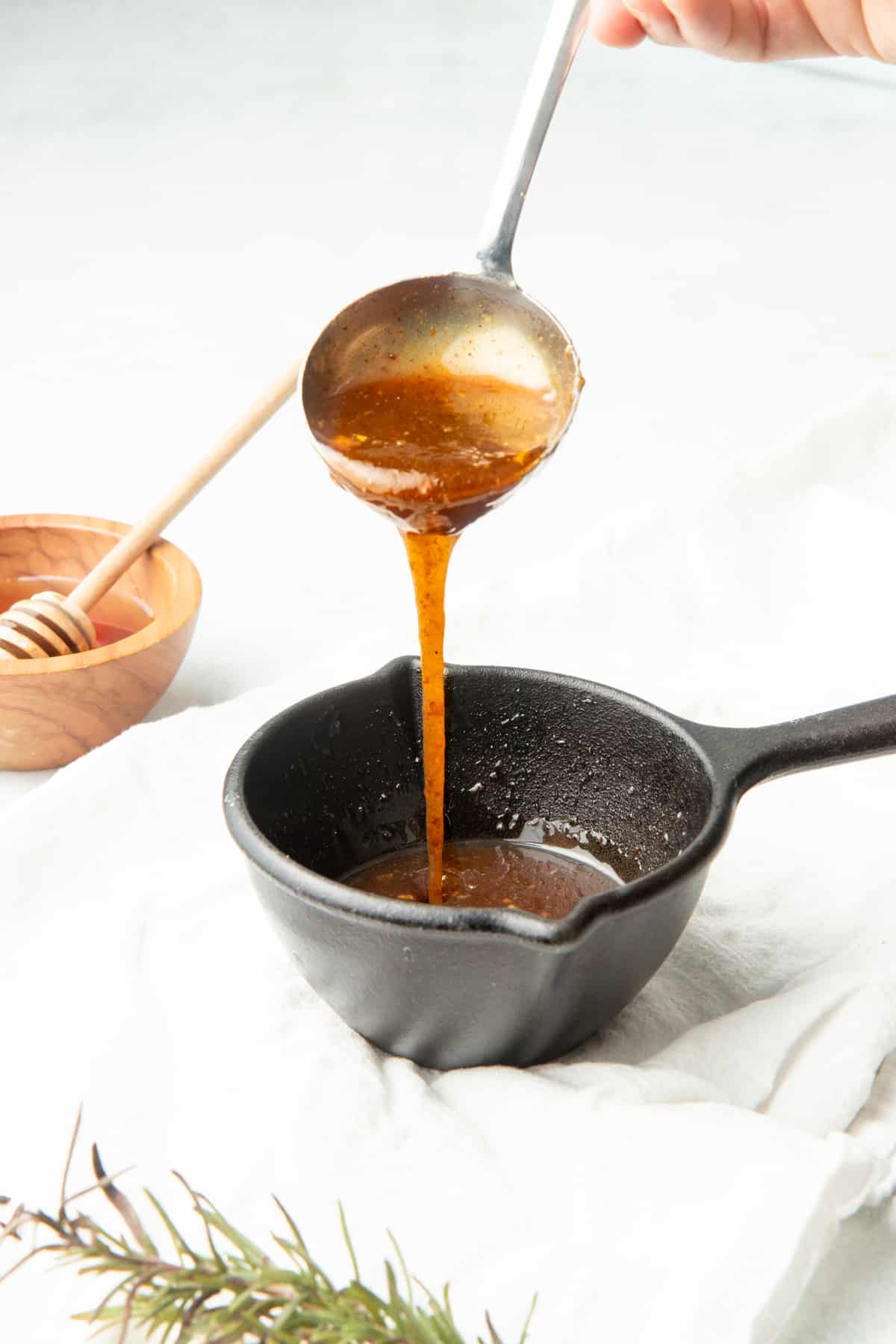 A silver serving spoon pours glaze into a small cast iron dish.