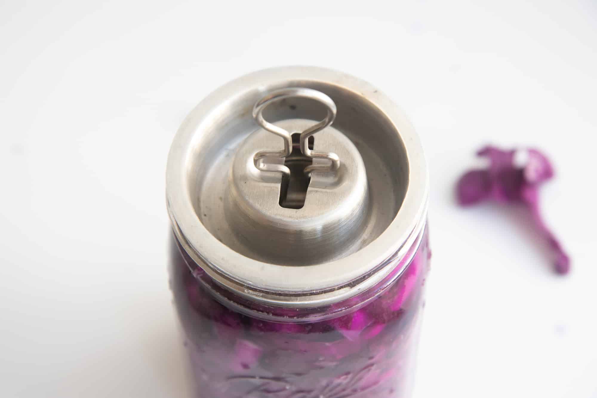 A fermentation lid sits on top of a glass jar of homemade sauerkraut.