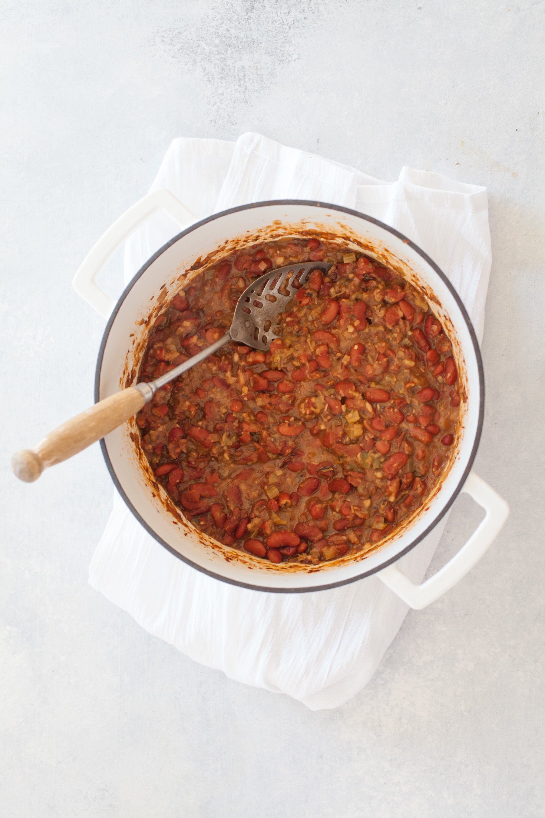 A pot full of cooked vegetarian red beans with a slotted spoon for serving