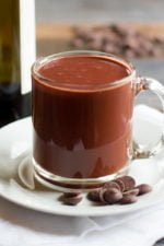 Clear glass mug of Red Wine Hot Chocolate on a white saucer with chocolate chips