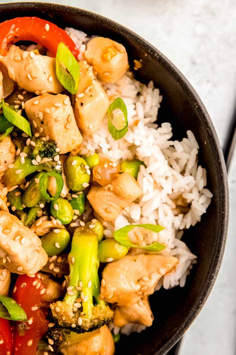 Close view of a homemade rice bowl topped with white meat and vegetables in a Japanese-inspired sauce.