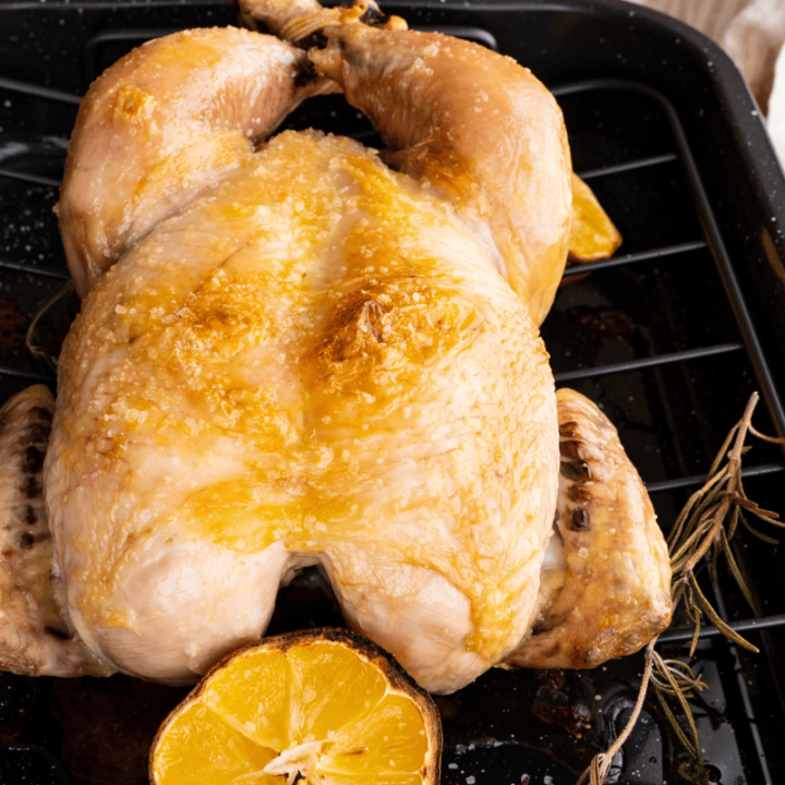 Poultry in a black roasting pan with a halved lemon and rosemary sprig