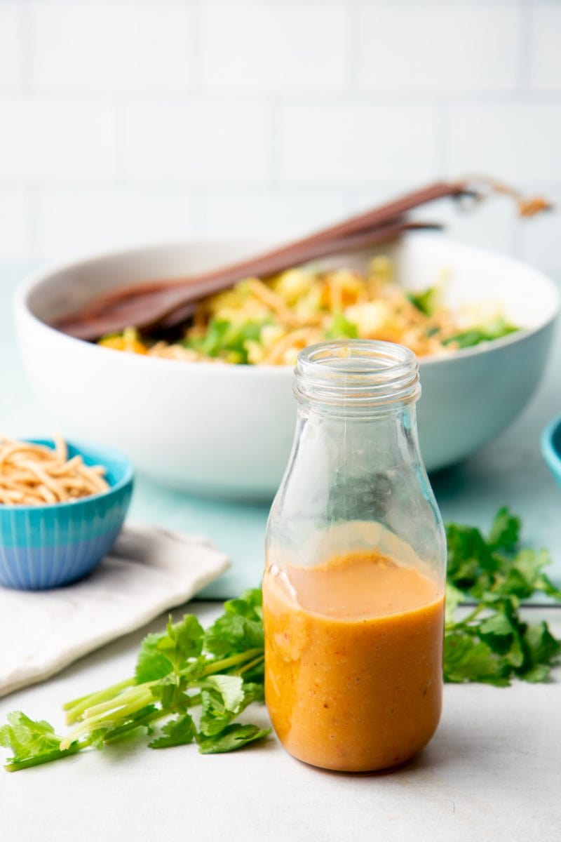 Homemade salad dressing in a glass bottle with fresh cilantro lying beside it.