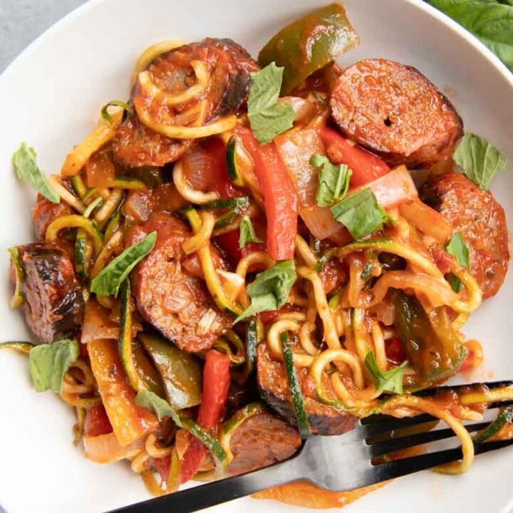 Close view of sausage and peppers served with zoodles on a round white plate.