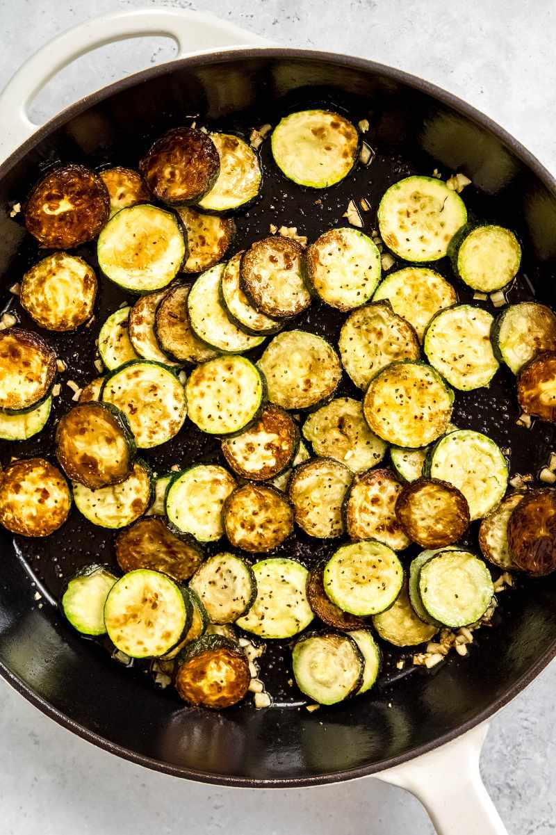 Top view of sauteed zucchini and garlic in an enameled cast iron skillet.