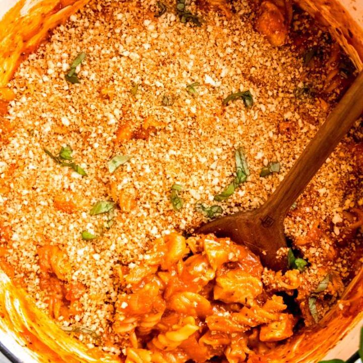 Overhead view of a wooden spoon scooping chicken parmesan pasta from a white enameled dutch oven.