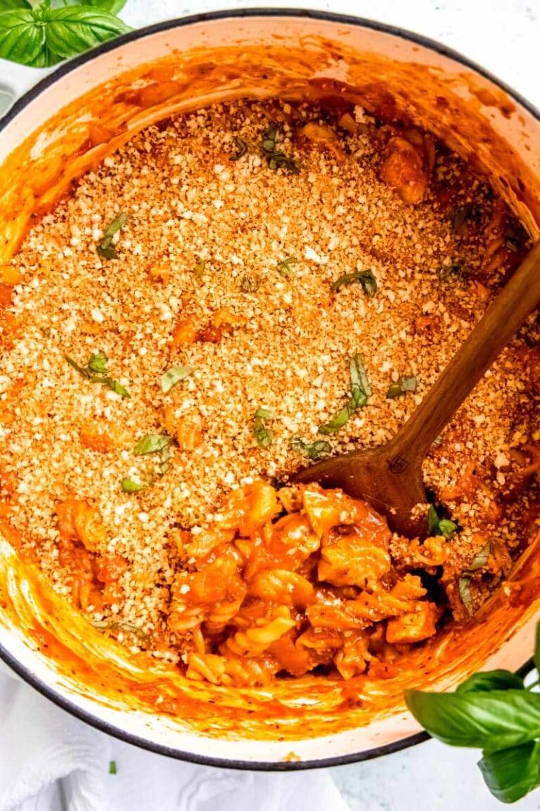 Overhead view of a wooden spoon scooping chicken parmesan pasta from a white enameled dutch oven.