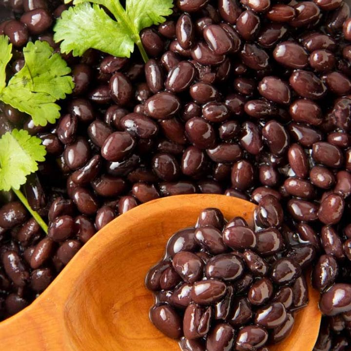 Close up of a wooden spoon scooping cooked black beans.