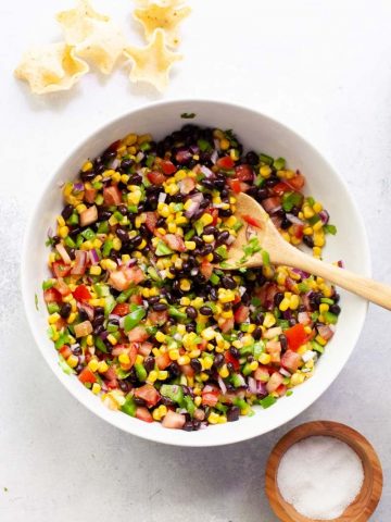 Overhead of a white serving bowl with black bean and corn salsa and a wooden spoon in it.