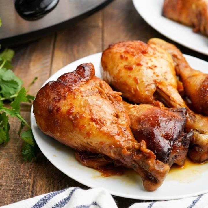 Crockpot chicken legs on a plate with a blue and white cloth napkin nearby.