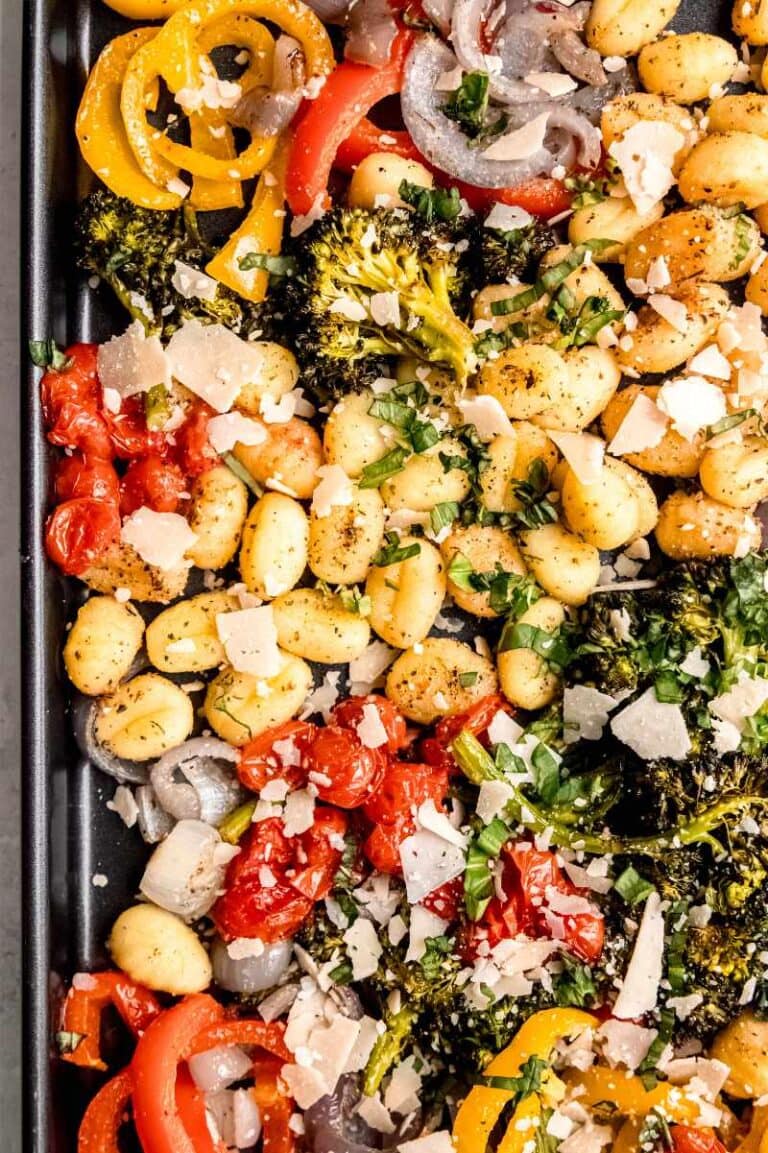 Top view of a dark sheet pan filled with baked gnocchi and vegetables topped with fresh basil and parmesan cheese.