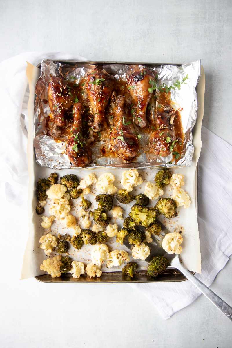 Overhead of a sheet pan dinner of sticky chicken drumsticks and sesame roasted broccoli and cauliflower.