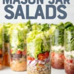 Tall mason jars sit on a white surface in front of a white wall. The jars are layered with salad ingredients. The jar in the front includes dressing, black beans, onions, tomatoes, and lettuce. Text overlay reads, "The Ultimate Guide to Mason Jar Salads."