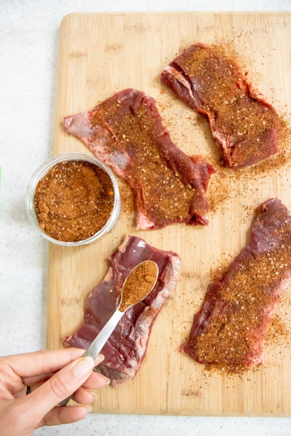 Hand spooning spice rub over raw skirt steak