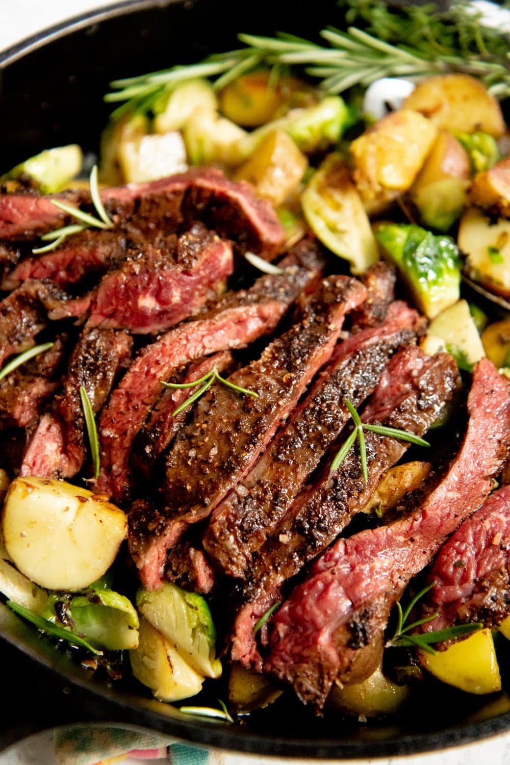 Sliced seared steak on top of Potatoes and Brussels sprouts in a cast iron skillet