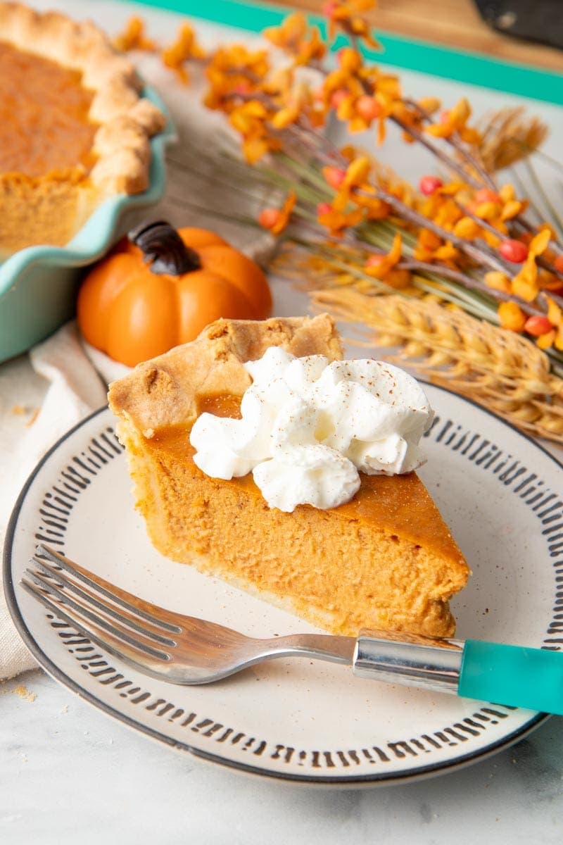 A single slice of pumpkin pie garnished with whipped cream sits on a plate with a teal-handled fork.