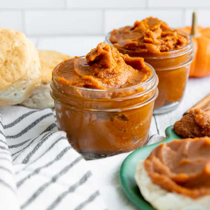 Two glass jars filled with Slow Cooker Pumpkin Butter, next to biscuits and a plate