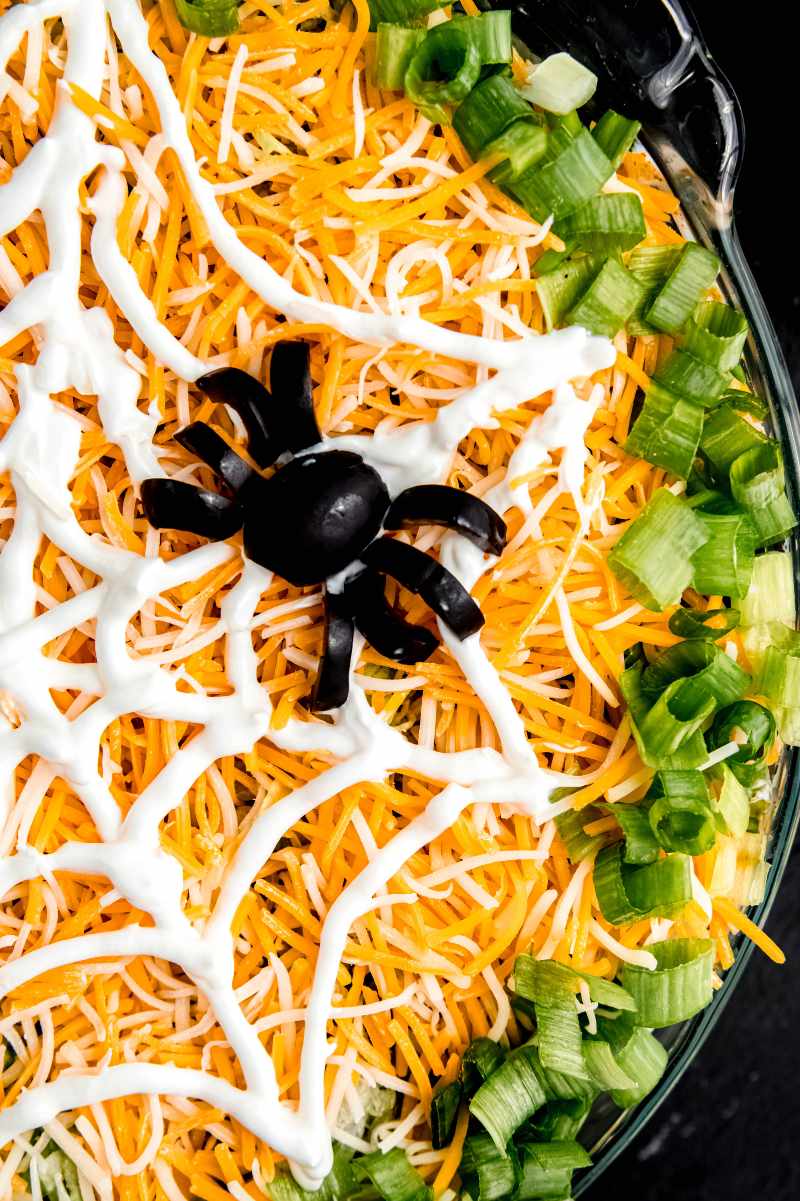 Close view of the sour cream cobweb topping and black olive spider on a Halloween appetizer.