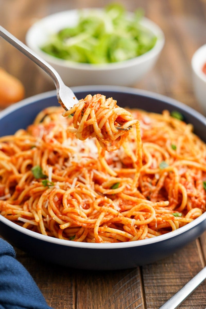 A fork wrapped in a tangle of spaghetti strands raised over a bowl of pasta arrabbiata.