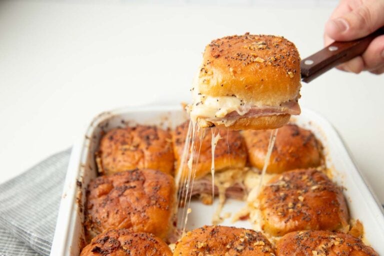 Close view of a spatula lifting a baked slider from a baking dish with strands of melted cheese stretching back to the pan.