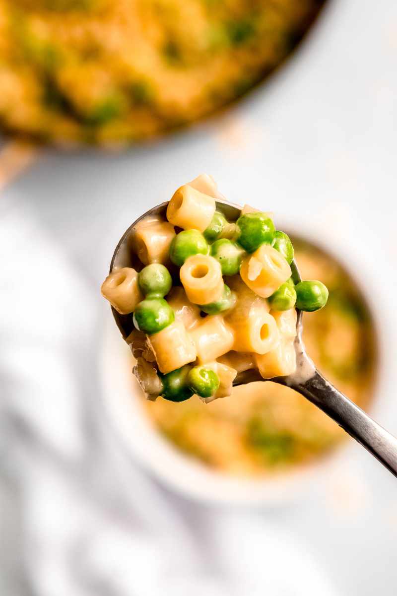 Tight view of a spoonful of creamy peas and ditalini garnished with parmesan.