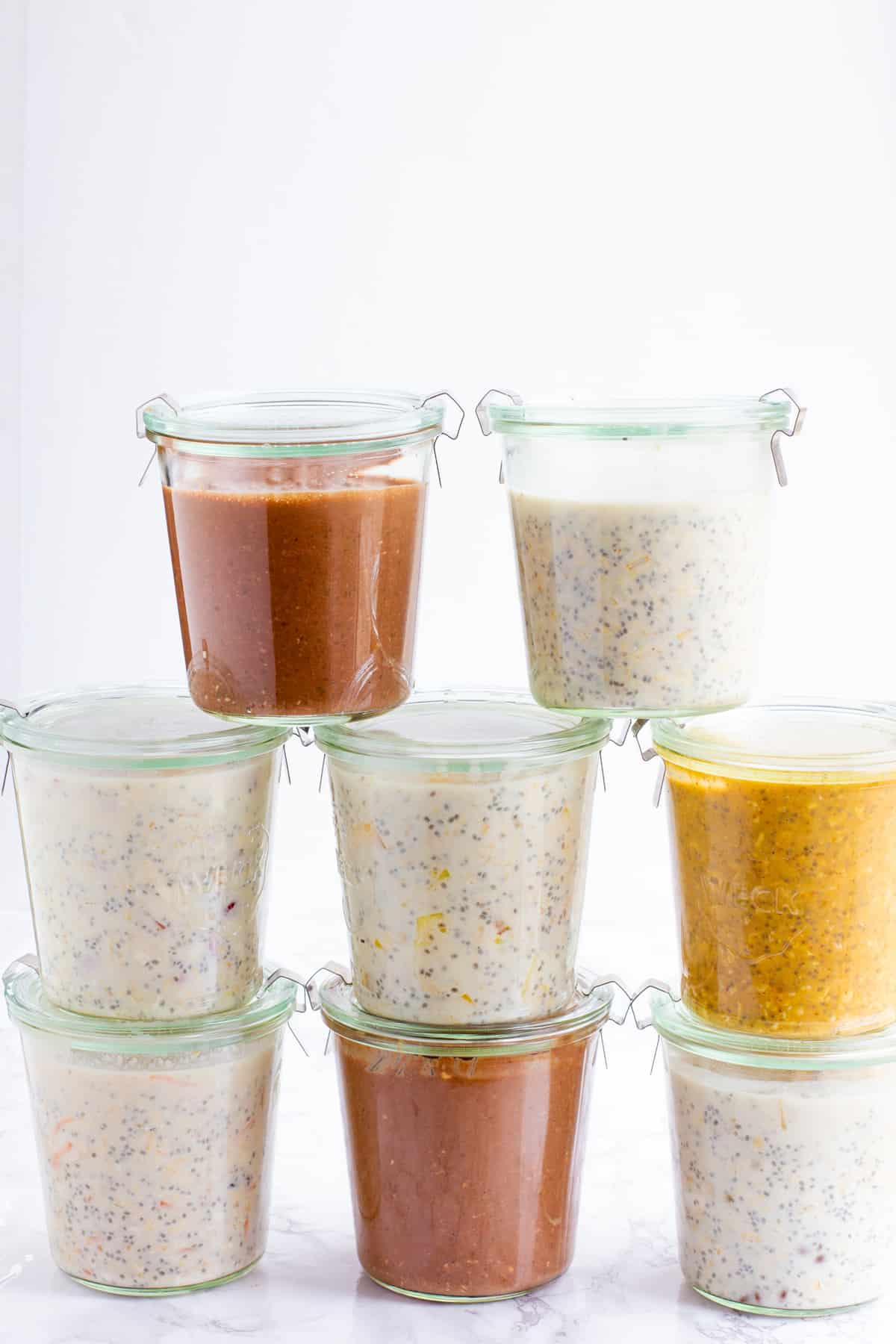 8 glass jars filled with different flavors of overnight oats stacked in a pyramid.