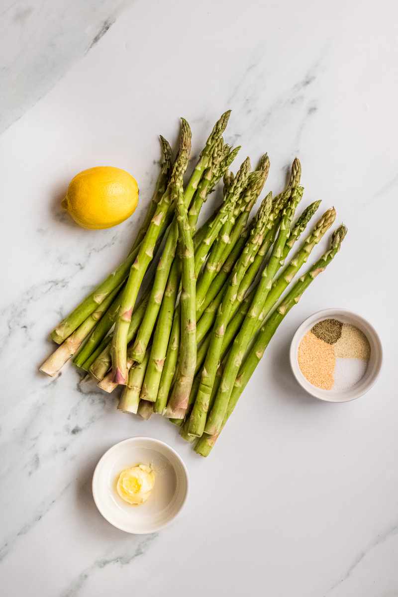 Overhead of ingredients needed to make steamed asparagus, including fresh spears, lemon, and seasoning.