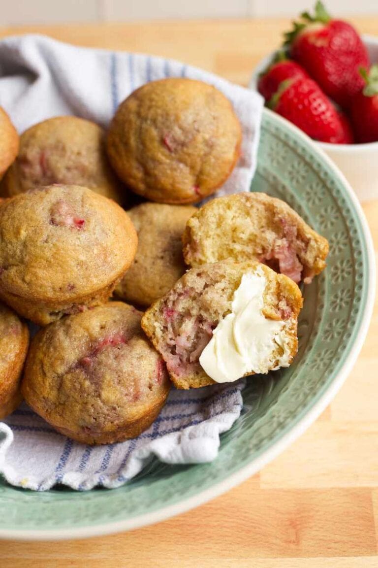 A bowl of strawberry muffins. One muffin is cut in half and smeared with butter.