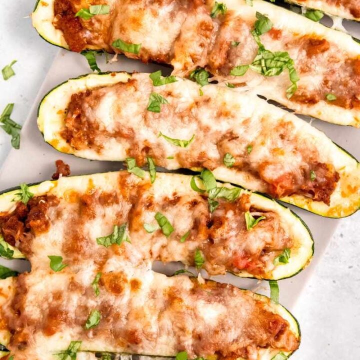 Close view of stuffed zucchini on a long white serving platter garnished with chopped fresh basil.