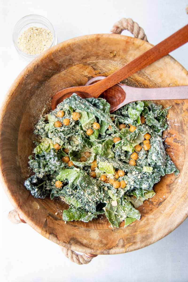 A large wooden bowl with kale caesar salad and crunchy chickpeas tossed in a homemade caesar dressing.